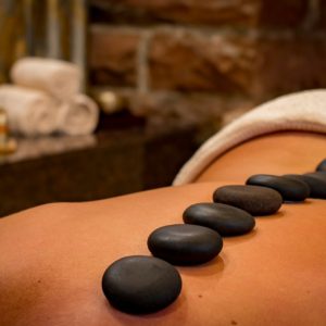 Close-up of smooth black stones placed in a line on a person's back in a spa setting. Towels and massage oils are blurred in the warm-toned background. Relaxing ambiance.