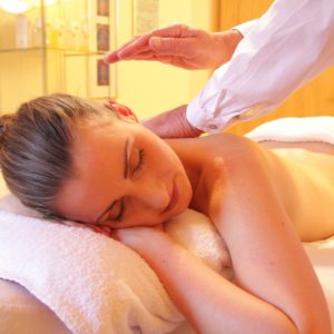 A woman enjoying a relaxing massage in a spa, eyes closed, lying on her side with a towel covering her lower body. Warm lighting creates a calming ambiance.