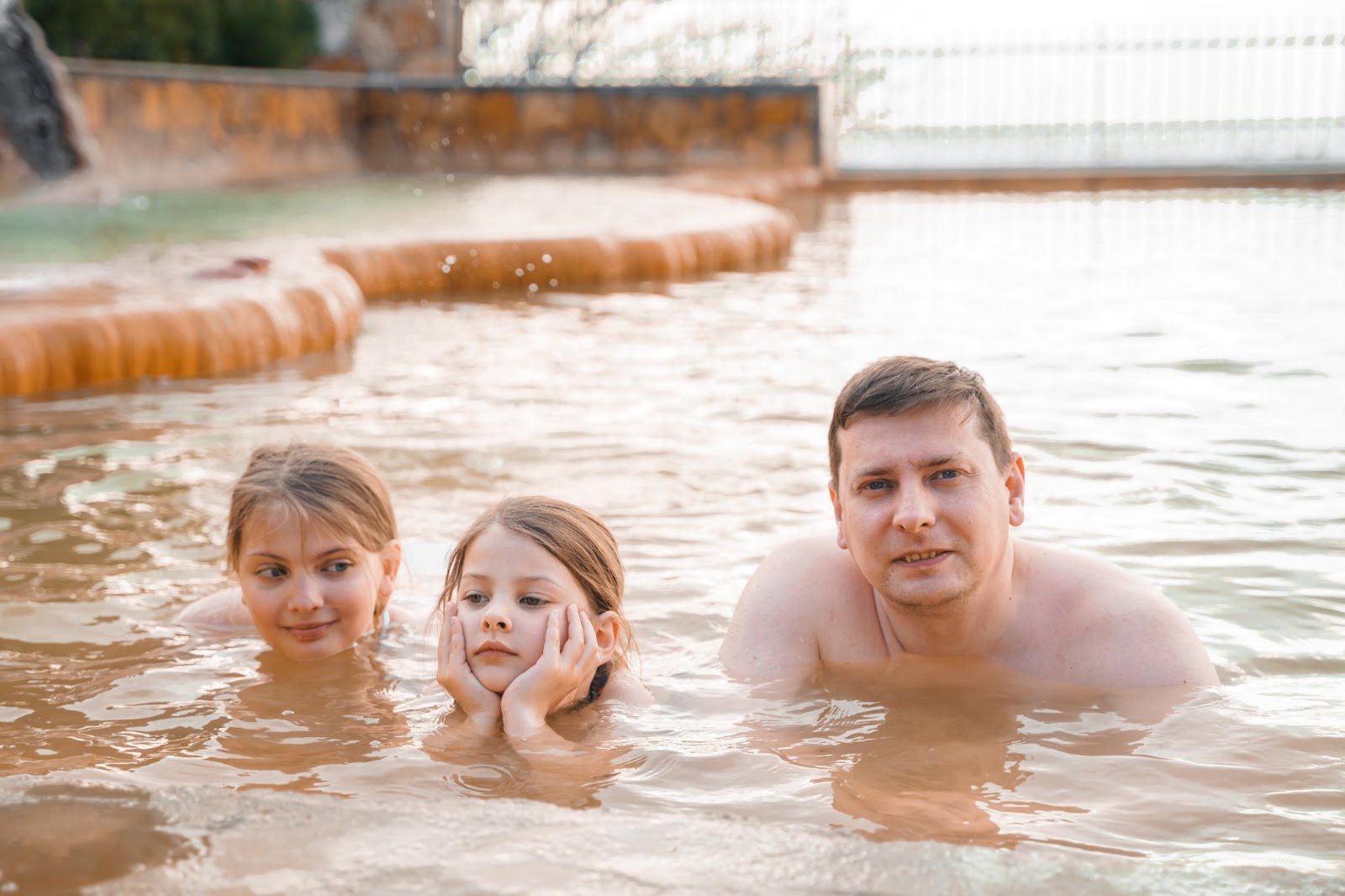 A man and two children play together in a swimming pool, enjoying a sunny day and splashing water around.