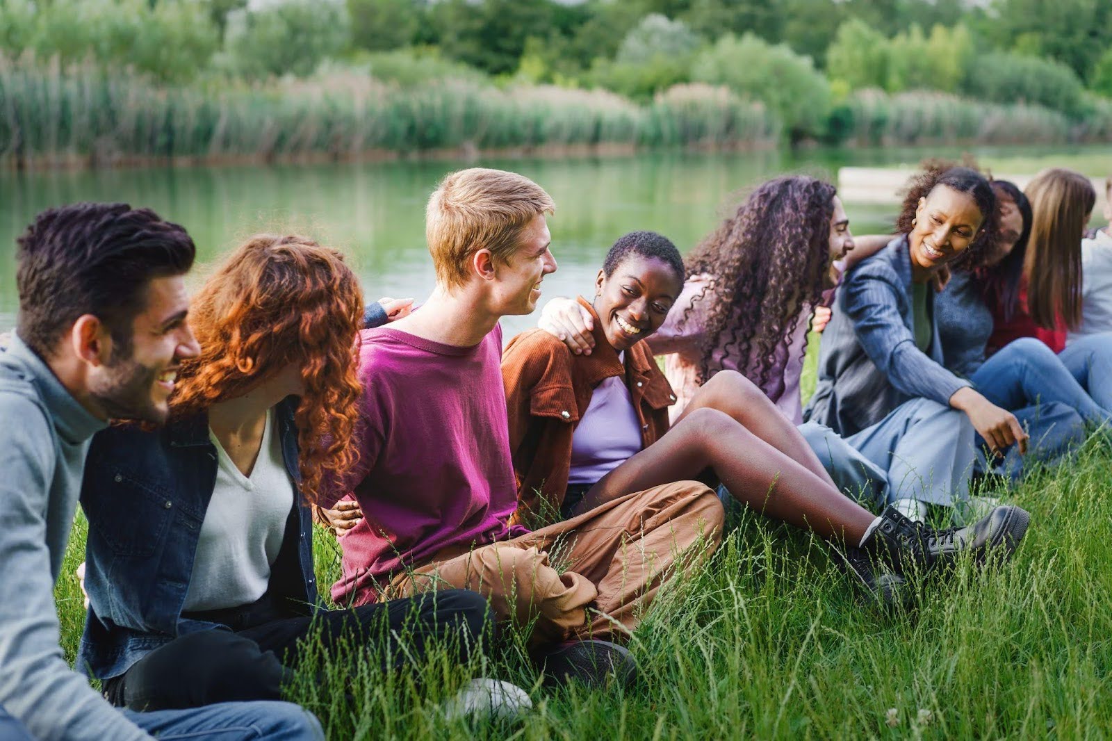 A group of young people relaxes on the grass by the river enjoying a sunny day together