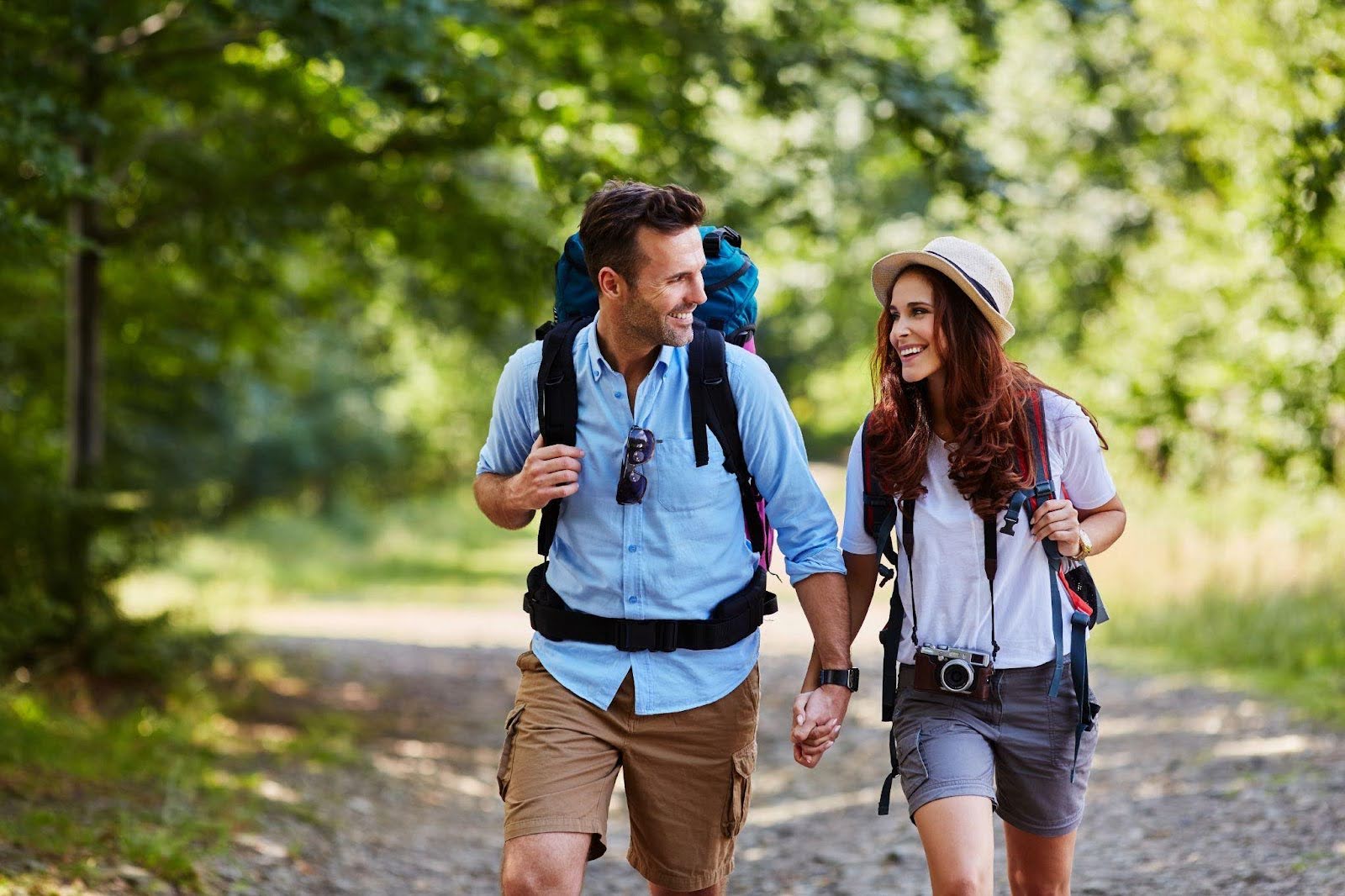 A man and woman hike on a nature trail both carrying backpacks enjoying the outdoors together