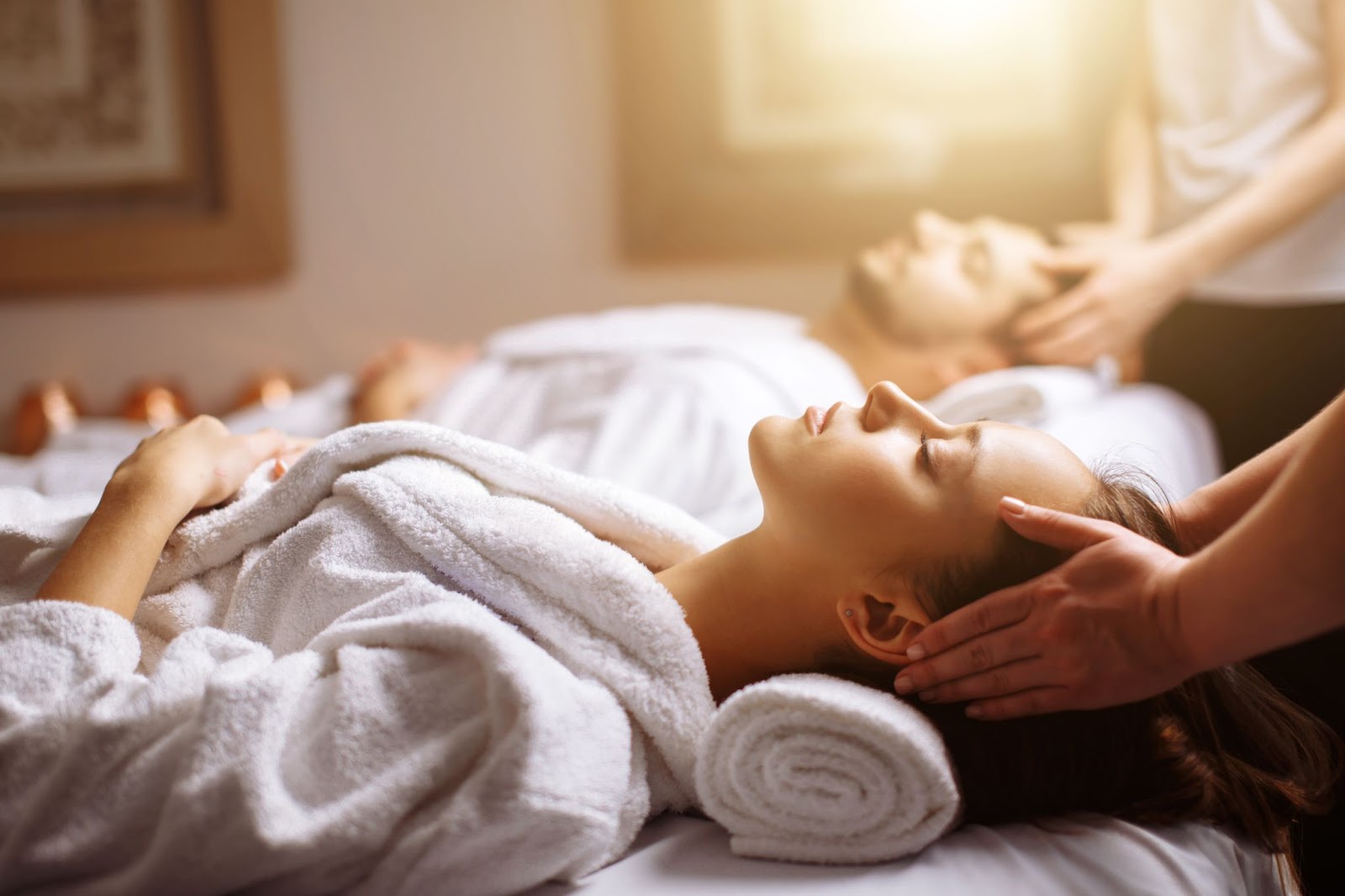 Couple relaxing during head massage at spa, wearing white robes