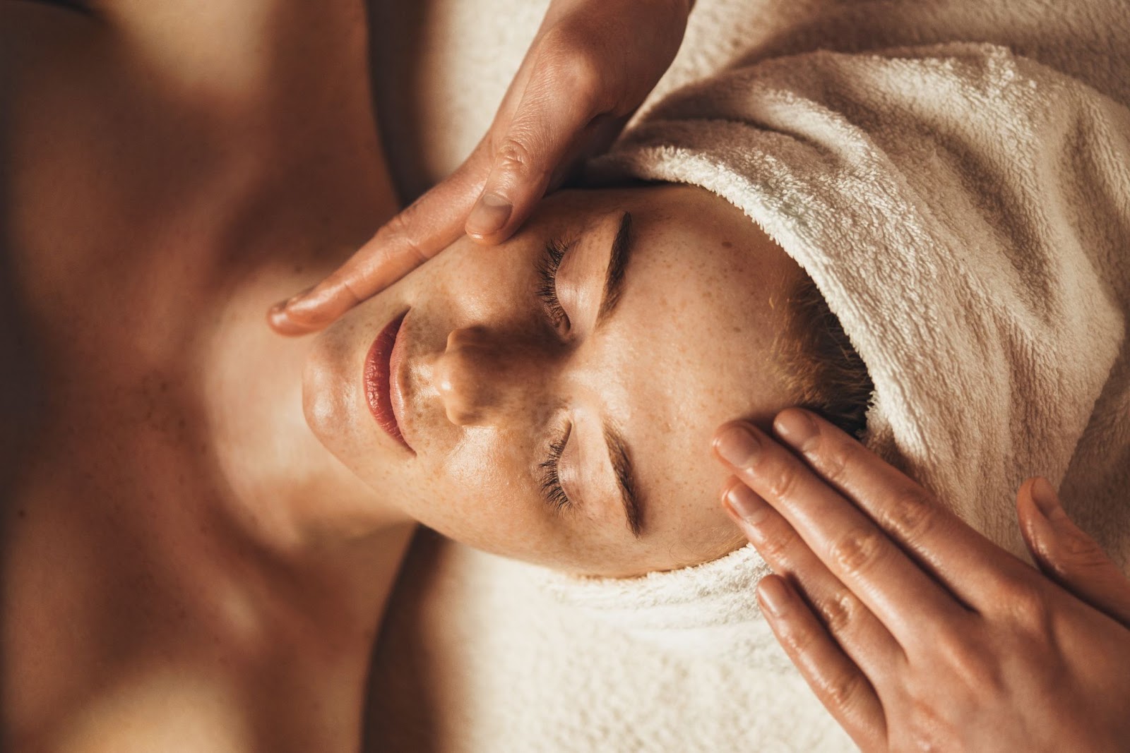 Person receiving a relaxing facial massage with a towel wrapped around head.