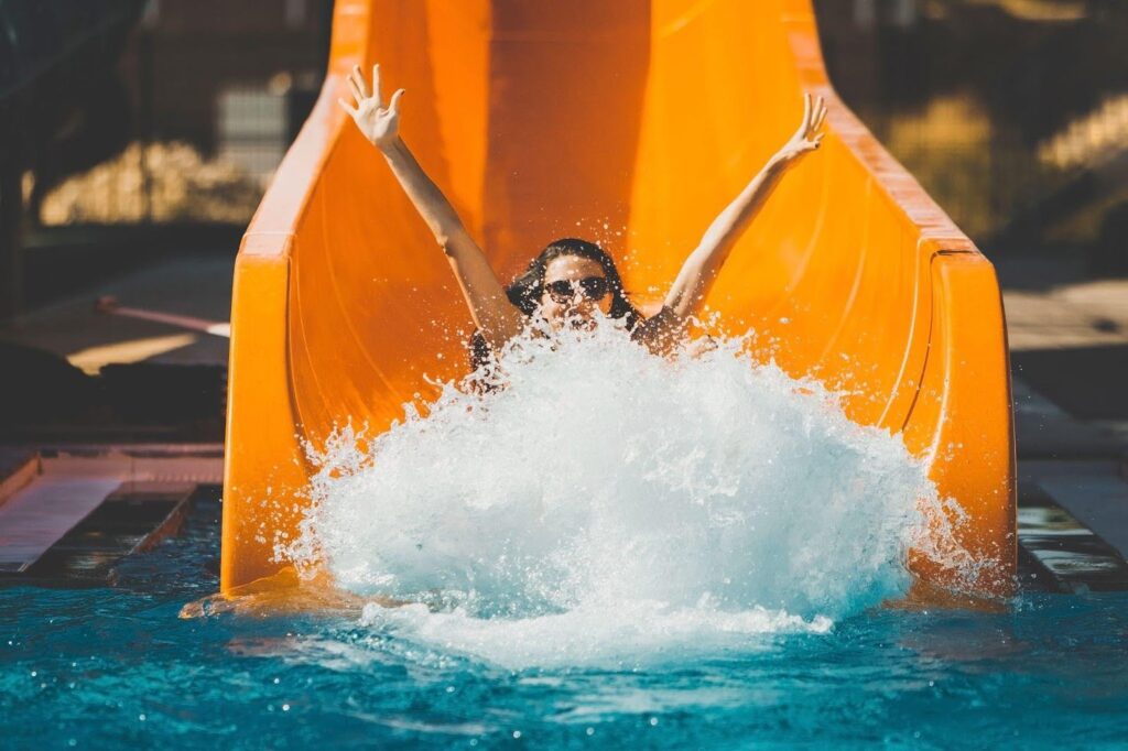 A woman joyfully slides down a colorful water slide splashing into the pool below