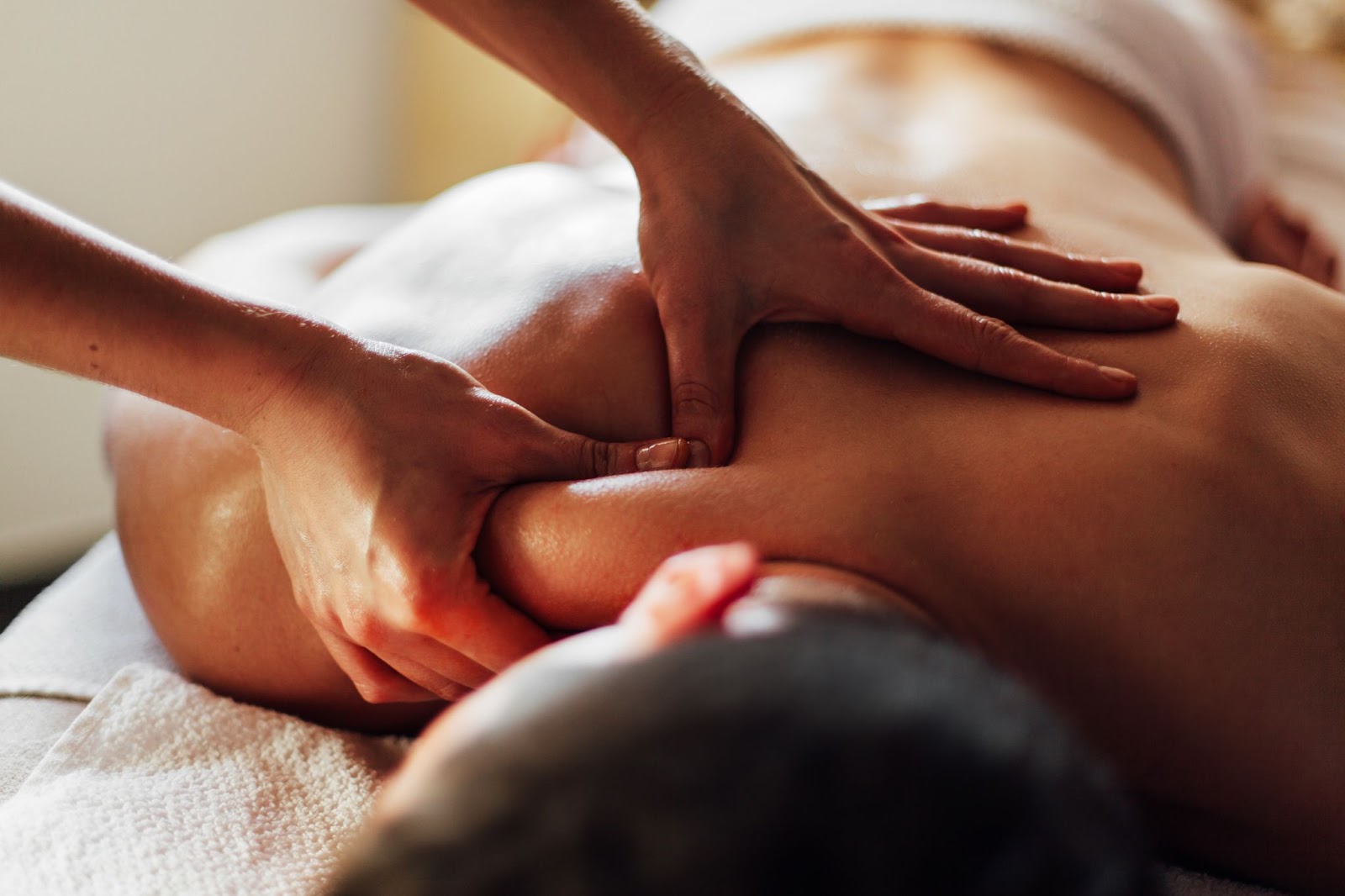 A close-up of a person receiving a professional deep tissue back massage, with a focus on the therapist's hands applying pressure to the shoulder and upper back.